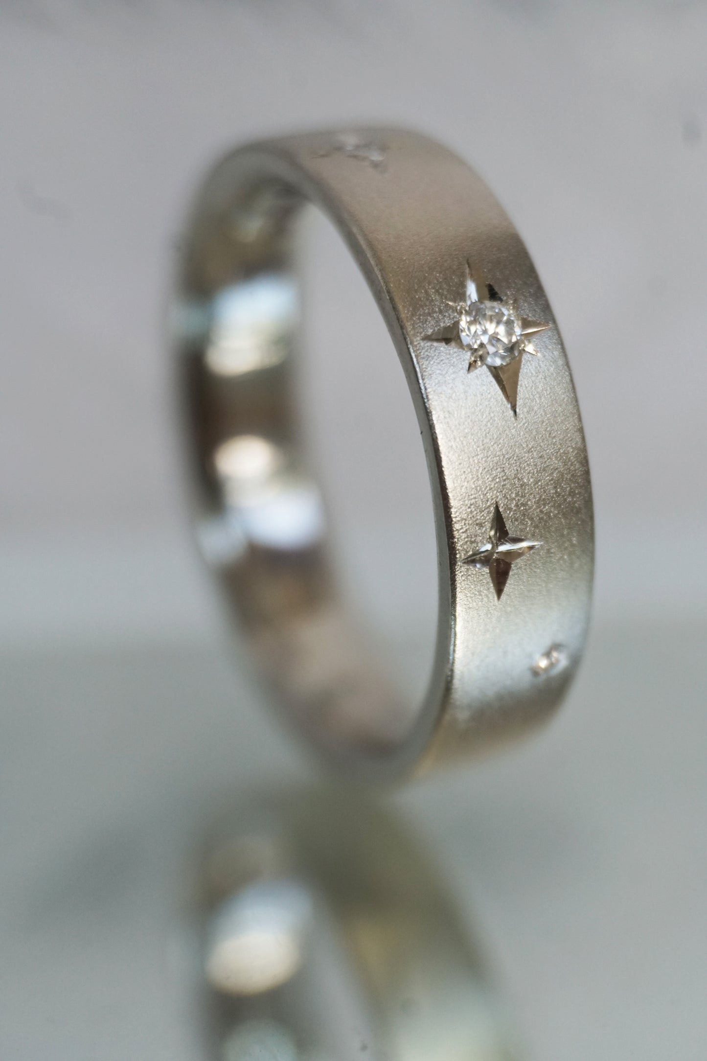 Close-up of Stellar Ring showing engraved starburst pattern and sparkling diamond detail on brushed silver surface.