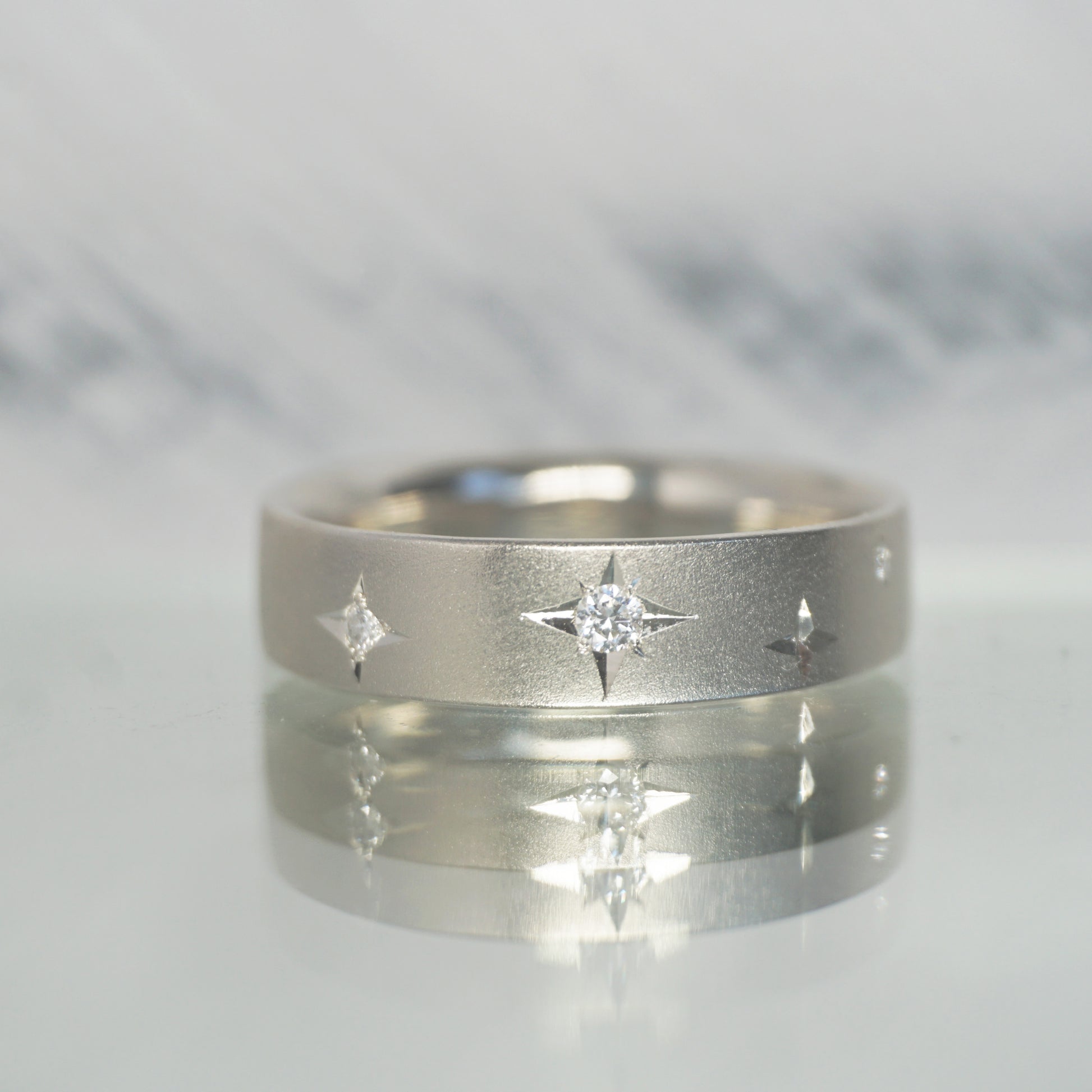 Close-up of Stellar Ring showing engraved starburst pattern and sparkling diamond detail on brushed silver surface.
